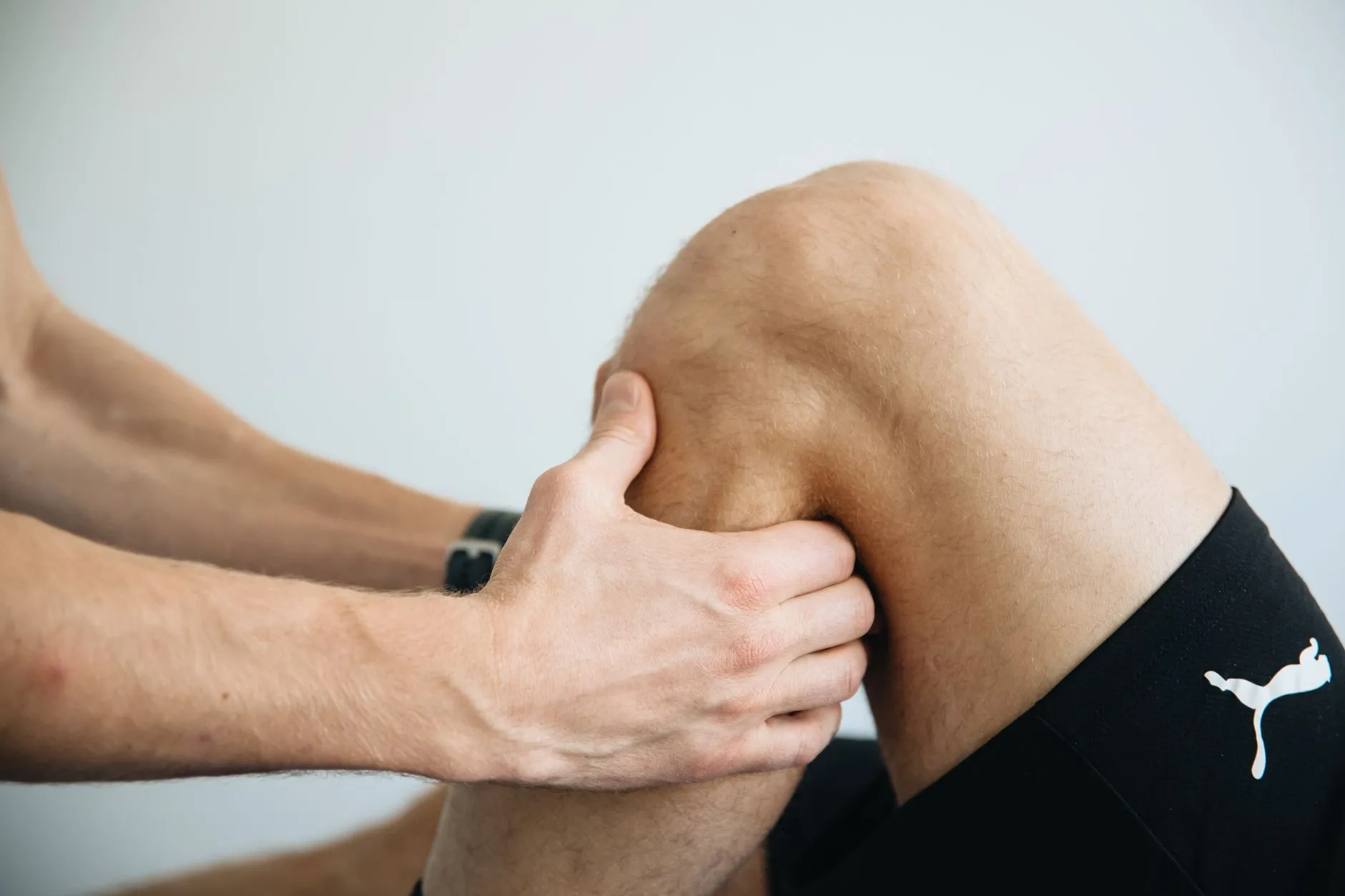 Fisioterapeuta examina com as mãos a parte de trás do joelho dobrado de um paciente