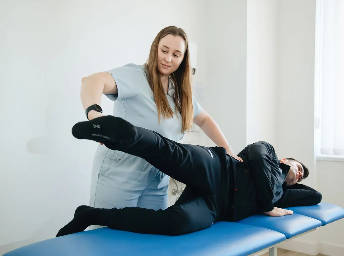 Fisioterapeuta orienta exercício de elevação da perna com paciente deitado de lado na maca